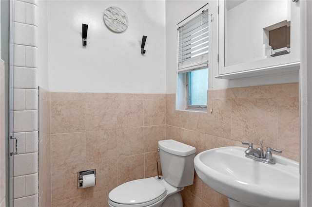 half bathroom with a sink, toilet, tile walls, and wainscoting