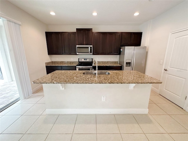 kitchen with light tile patterned floors, a breakfast bar, a kitchen island with sink, a sink, and appliances with stainless steel finishes