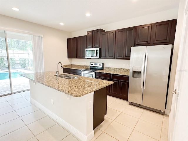 kitchen with dark brown cabinetry, an island with sink, light tile patterned floors, stainless steel appliances, and a sink