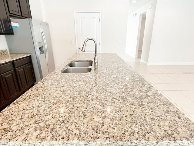 kitchen with light tile patterned floors, light stone countertops, a sink, dark brown cabinets, and stainless steel refrigerator with ice dispenser