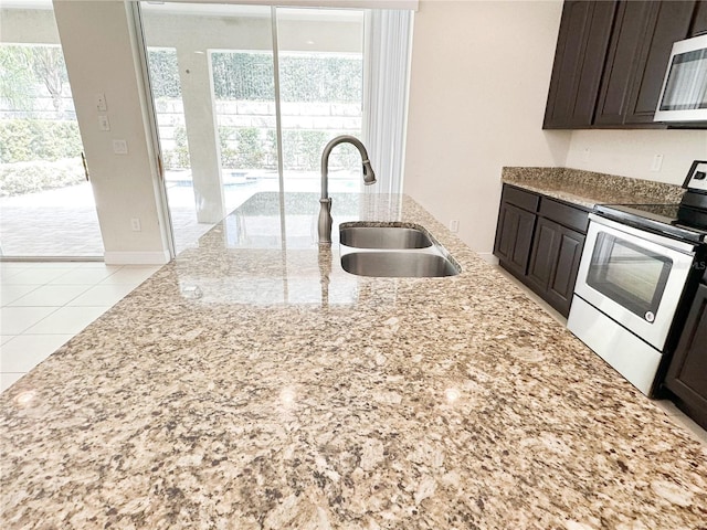 kitchen featuring a sink, light stone counters, dark brown cabinetry, appliances with stainless steel finishes, and baseboards