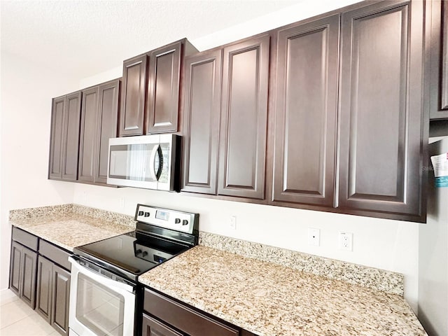 kitchen featuring dark brown cabinetry, appliances with stainless steel finishes, light stone counters, and light tile patterned flooring