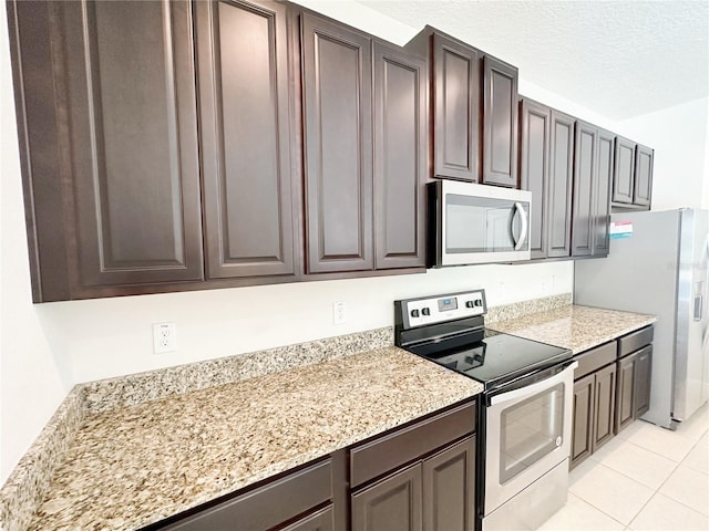 kitchen featuring light stone counters, light tile patterned flooring, dark brown cabinetry, appliances with stainless steel finishes, and a textured ceiling