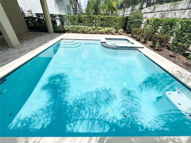 view of swimming pool featuring a pool with connected hot tub and fence