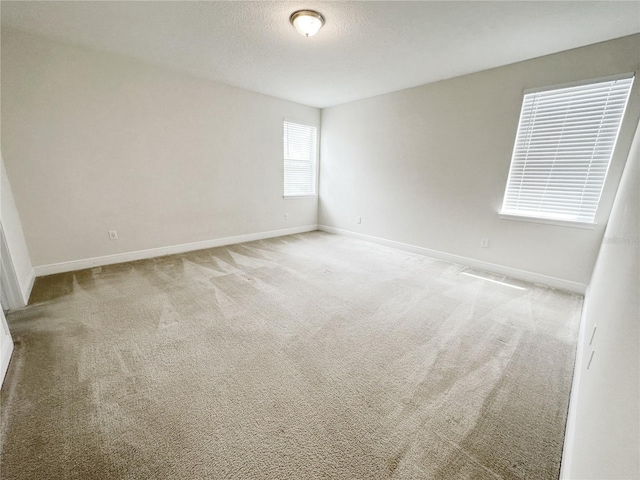 empty room with light colored carpet, a textured ceiling, and baseboards