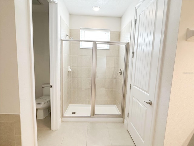 bathroom featuring a shower stall, toilet, tile patterned floors, and a textured ceiling