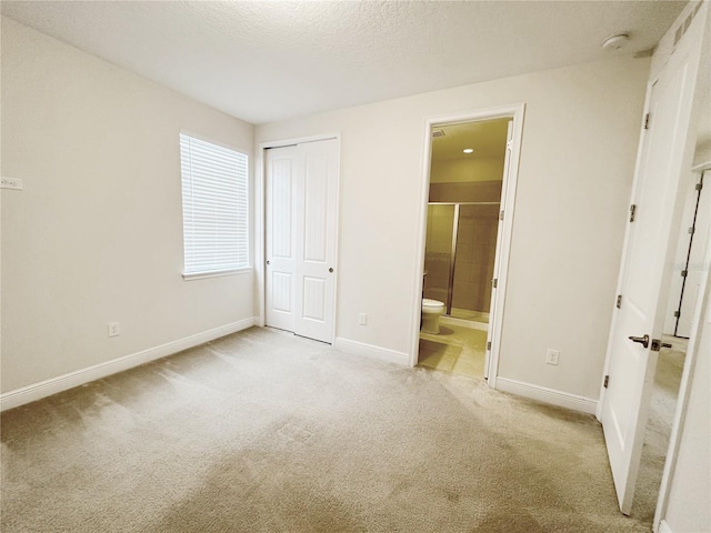 unfurnished bedroom featuring carpet, baseboards, a closet, ensuite bathroom, and a textured ceiling