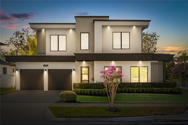 contemporary house featuring stucco siding, decorative driveway, and a front lawn