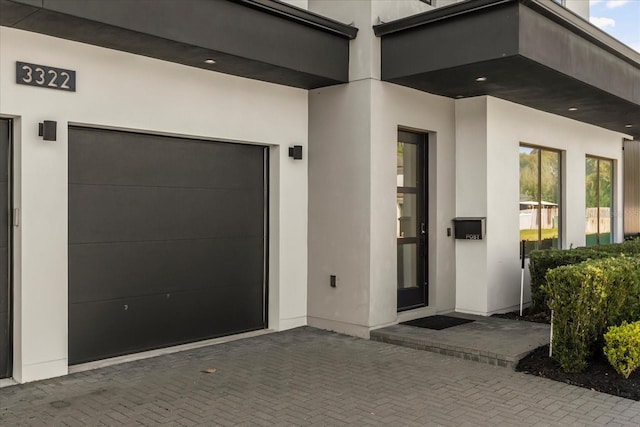 doorway to property featuring a garage, decorative driveway, and stucco siding