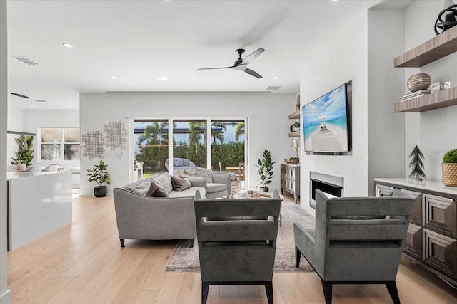 living area with a ceiling fan, visible vents, light wood-style flooring, recessed lighting, and a large fireplace