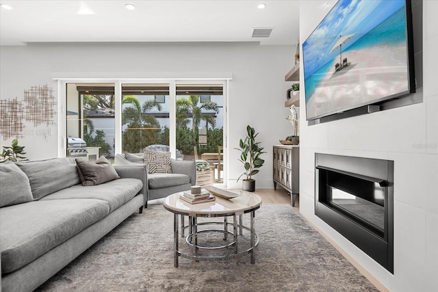 living room with a glass covered fireplace, wood finished floors, recessed lighting, and visible vents