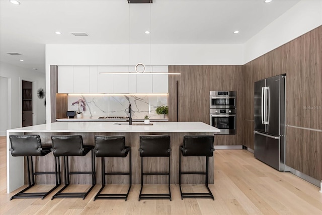 kitchen featuring backsplash, a breakfast bar area, light countertops, stainless steel appliances, and modern cabinets