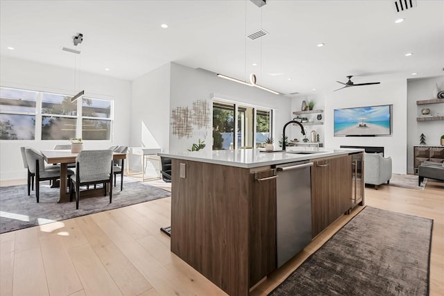 kitchen with a center island with sink, light wood-type flooring, stainless steel dishwasher, modern cabinets, and a sink