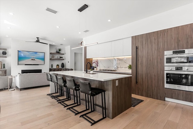 kitchen featuring stainless steel double oven, light wood-style floors, white cabinetry, modern cabinets, and tasteful backsplash