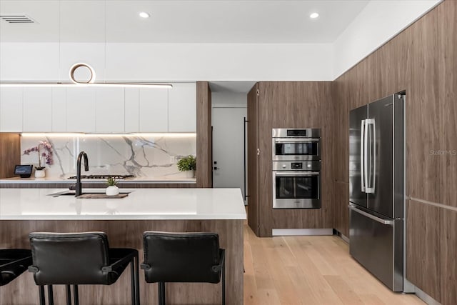 kitchen featuring light wood-style floors, appliances with stainless steel finishes, a kitchen breakfast bar, modern cabinets, and tasteful backsplash