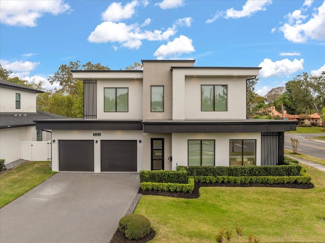 contemporary house featuring stucco siding, a front lawn, decorative driveway, fence, and an attached garage