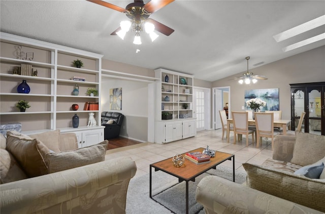 living area with visible vents, lofted ceiling with skylight, light tile patterned flooring, and a ceiling fan