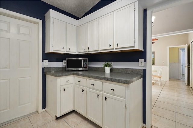 kitchen featuring stainless steel microwave, white cabinets, light tile patterned flooring, and dark countertops