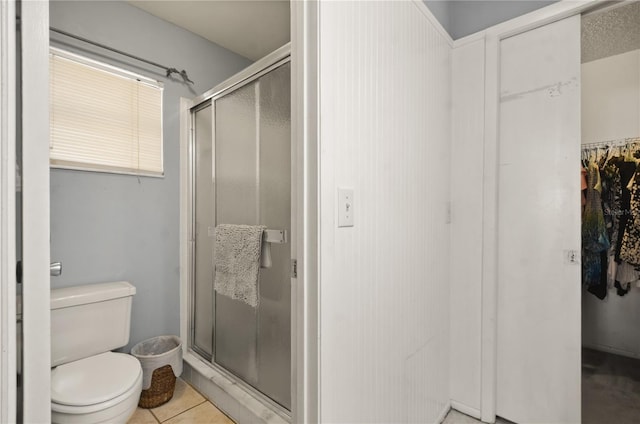 bathroom with tile patterned floors, toilet, a stall shower, and a spacious closet