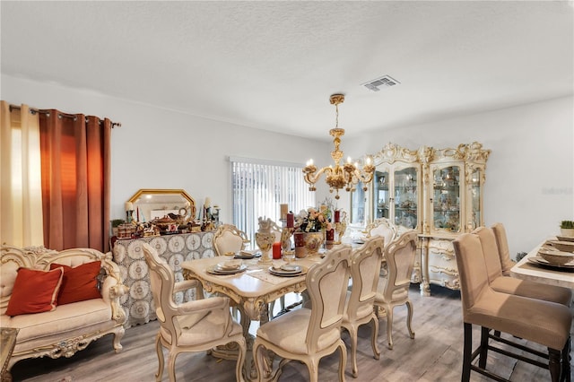 dining room featuring a textured ceiling, wood finished floors, visible vents, and a chandelier