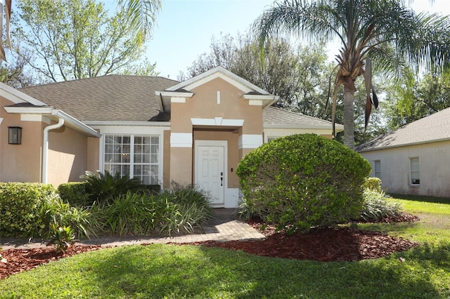 view of front facade featuring stucco siding, a front lawn, and a shingled roof