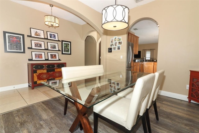 dining space featuring arched walkways, baseboards, and wood finished floors