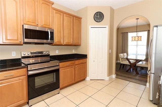 kitchen featuring baseboards, pendant lighting, dark stone counters, light tile patterned flooring, and stainless steel appliances