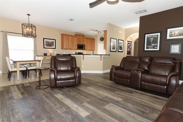 living room with visible vents, ceiling fan with notable chandelier, arched walkways, baseboards, and dark wood-style flooring