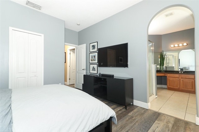 bedroom with visible vents, light wood-type flooring, a sink, a closet, and arched walkways