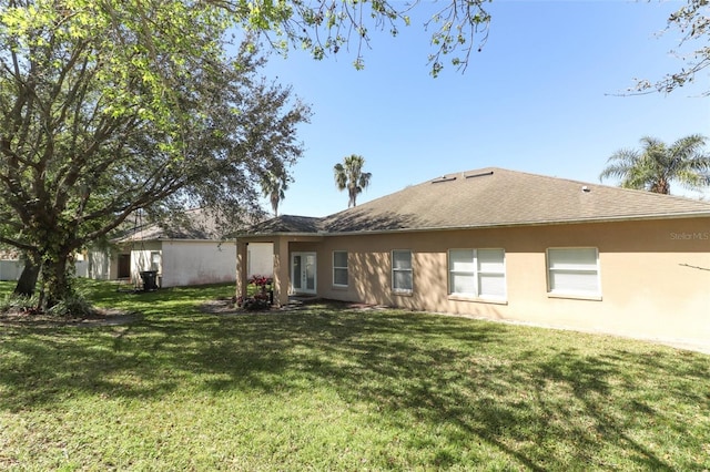 back of house with a shingled roof, a yard, french doors, and stucco siding