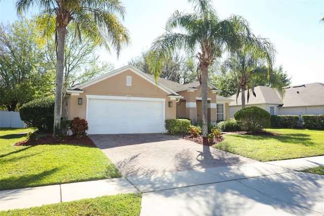 view of front facade featuring fence, a front yard, stucco siding, decorative driveway, and an attached garage