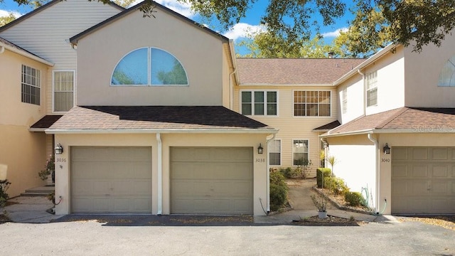 view of front facade featuring a garage, a shingled roof, and stucco siding