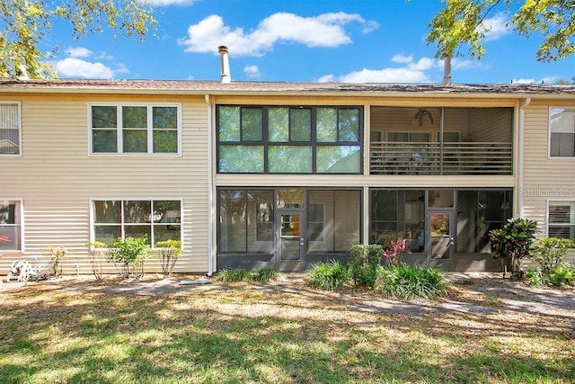 back of property featuring a balcony, a lawn, and a sunroom