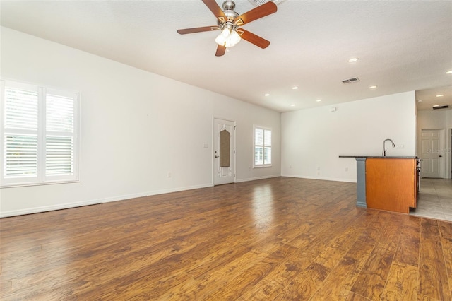 unfurnished living room with visible vents, a sink, wood finished floors, baseboards, and ceiling fan