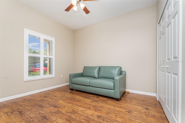 living area with baseboards, wood finished floors, and a ceiling fan