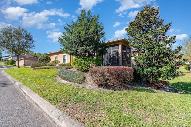 view of property hidden behind natural elements featuring a front lawn, a sunroom, and stucco siding