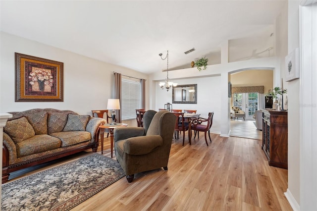 living room with visible vents, lofted ceiling, light wood-style floors, arched walkways, and a notable chandelier