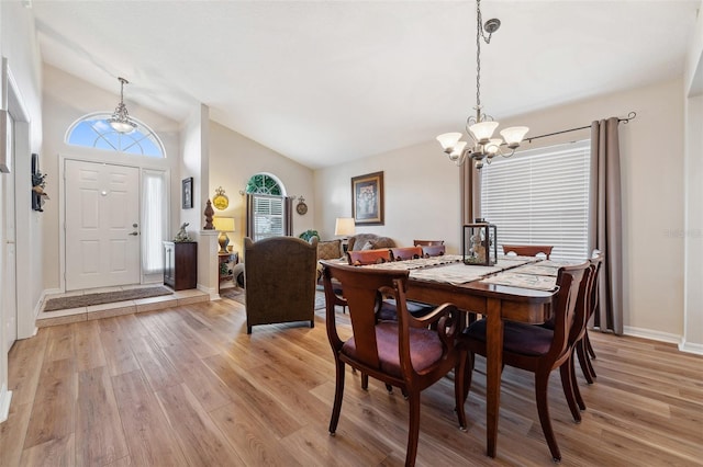 dining area with an inviting chandelier, light wood-style flooring, baseboards, and high vaulted ceiling