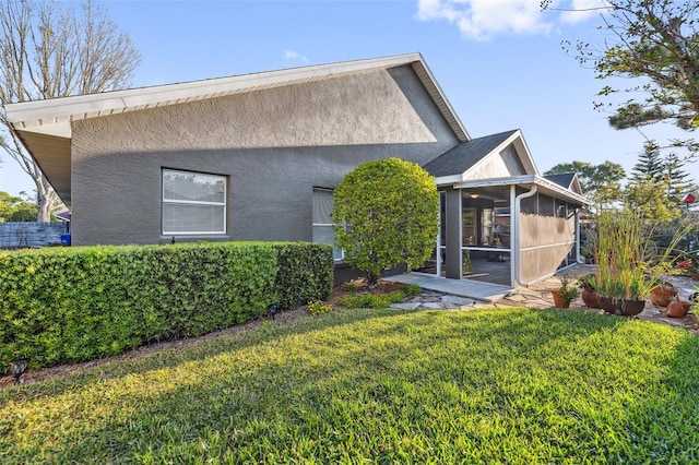 back of house with a lawn, a sunroom, and stucco siding