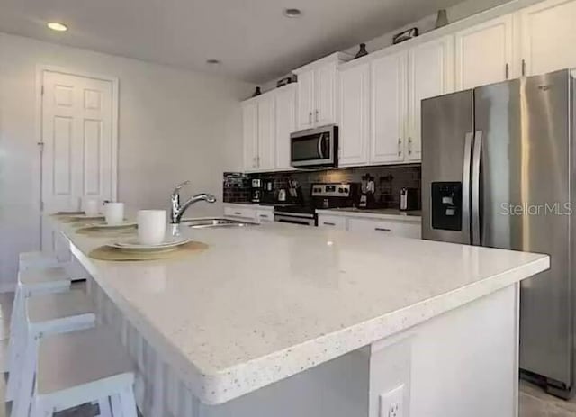 kitchen featuring a kitchen island with sink, decorative backsplash, white cabinets, stainless steel appliances, and a sink