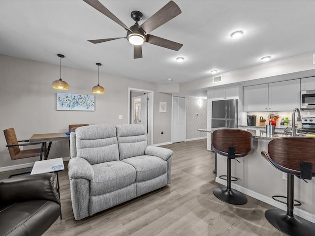 living room featuring visible vents, baseboards, light wood-style floors, and ceiling fan