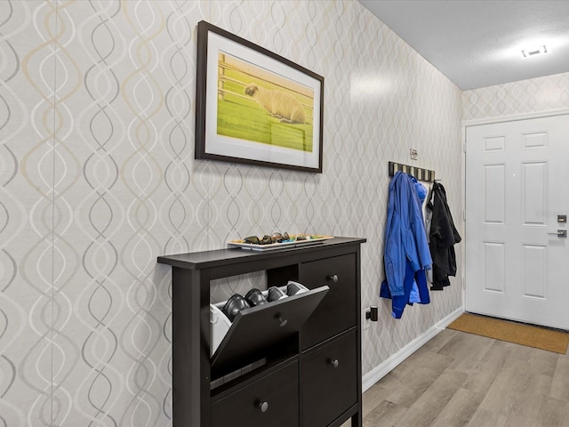 interior space with visible vents, wallpapered walls, baseboards, light wood-type flooring, and a textured ceiling