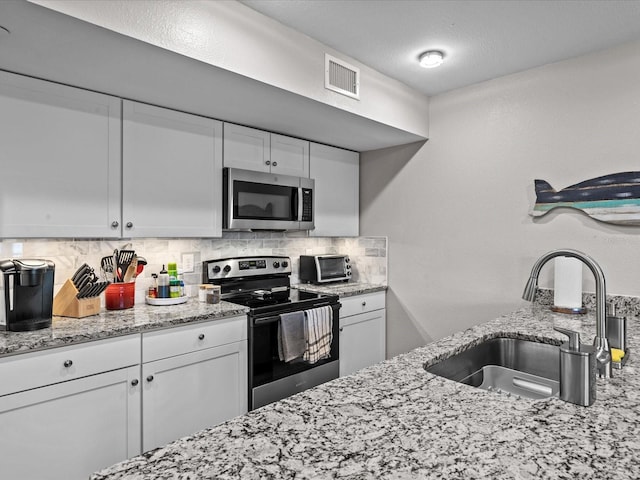 kitchen featuring visible vents, a sink, decorative backsplash, stainless steel appliances, and white cabinetry