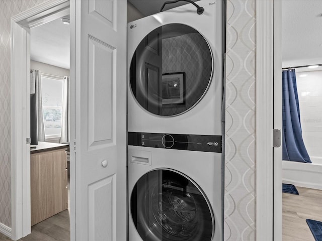 clothes washing area featuring laundry area, stacked washer / drying machine, and wood finished floors