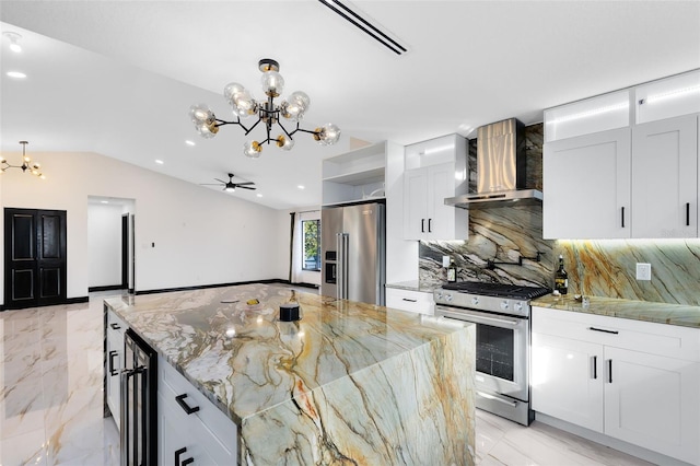 kitchen featuring lofted ceiling, stainless steel appliances, white cabinetry, wall chimney range hood, and marble finish floor