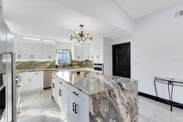 kitchen with tasteful backsplash, marble finish floor, appliances with stainless steel finishes, and a chandelier