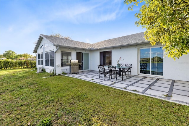 rear view of property with stucco siding, a lawn, a shingled roof, and a patio area