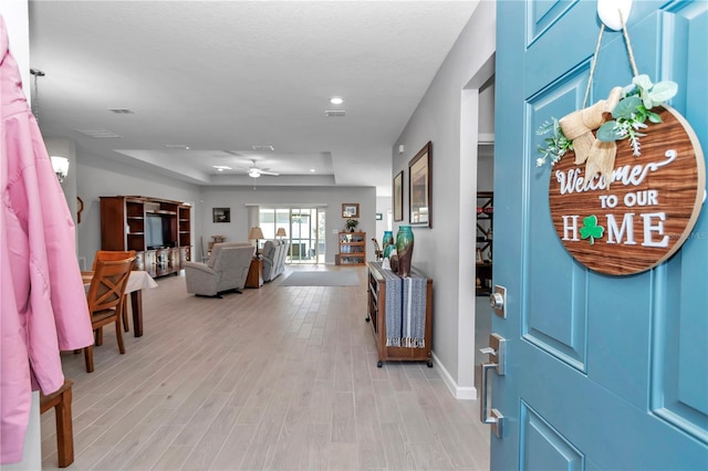 foyer with ceiling fan, baseboards, a tray ceiling, recessed lighting, and light wood-style floors