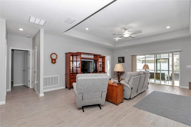 living area with visible vents, ceiling fan, a tray ceiling, and light wood-style floors