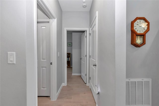 hallway with wood finish floors, visible vents, and baseboards